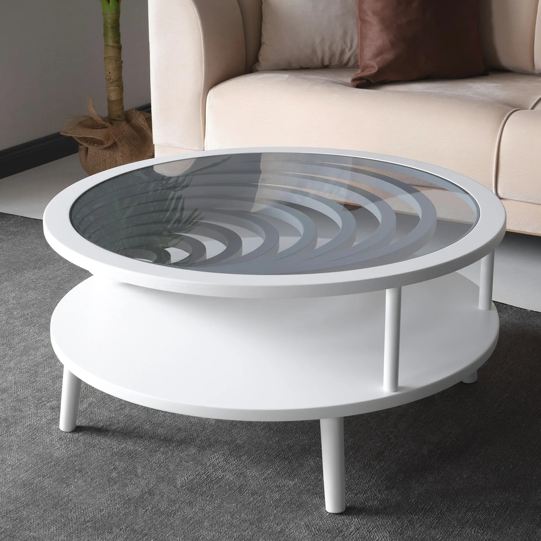 A modern white coffee table with a circular glass top and a lower shelf, placed on a grey carpet.