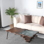 A stylish coffee table with a unique layered design, featuring wood and glass elements, placed in a living room setting with a white sofa and decorative pillows.
