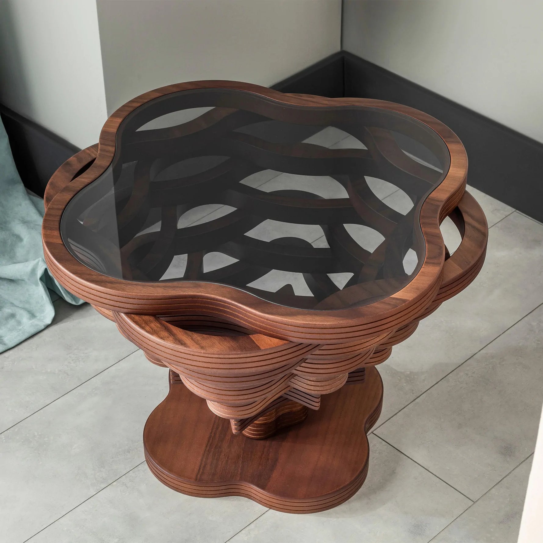 A cloud-shaped coffee table with a wooden structure and a glass top, featuring built-in handles and placed on a tiled floor.